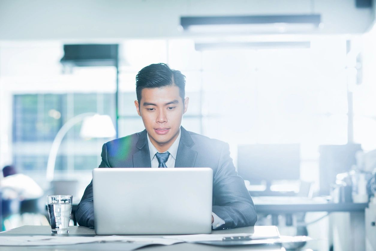 A man in suit and tie sitting at table with laptop.